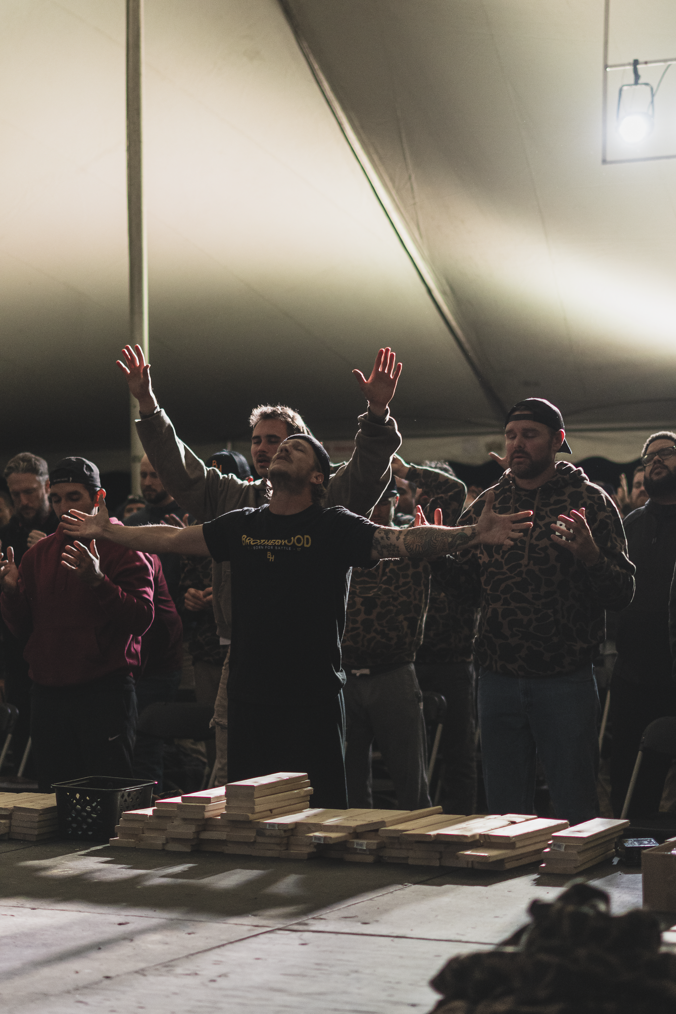 Men worshiping together under a tent at Brotherhood, arms outstretched.